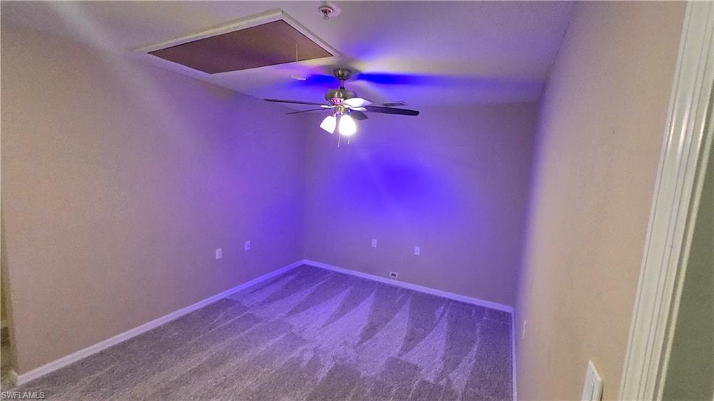 Spare room featuring attic access, dark colored carpet, and ceiling fan