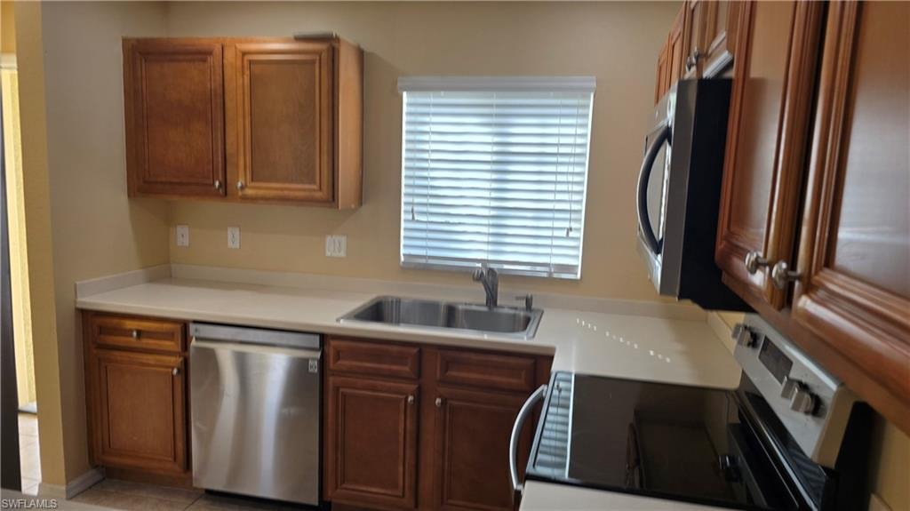 Kitchen featuring stainless steel appliances, light countertops, and brown cabinetry