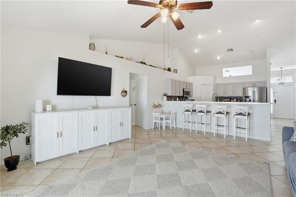 Living room featuring high vaulted ceiling, a ceiling fan, and light tile patterned flooring