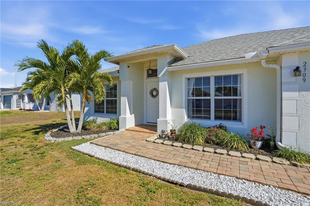 Doorway to property featuring a lawn, roof with shingles, and stucco siding