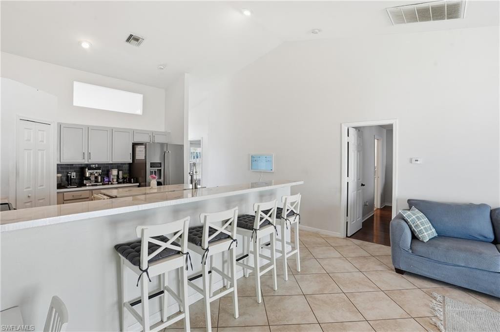 Kitchen featuring a kitchen bar, high vaulted ceiling, high end refrigerator, light tile patterned floors, and gray cabinetry