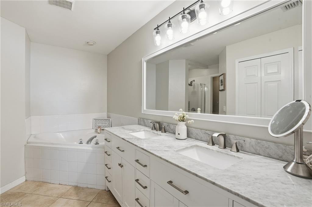Bathroom featuring a garden tub, a shower stall, double vanity, and light tile patterned floors
