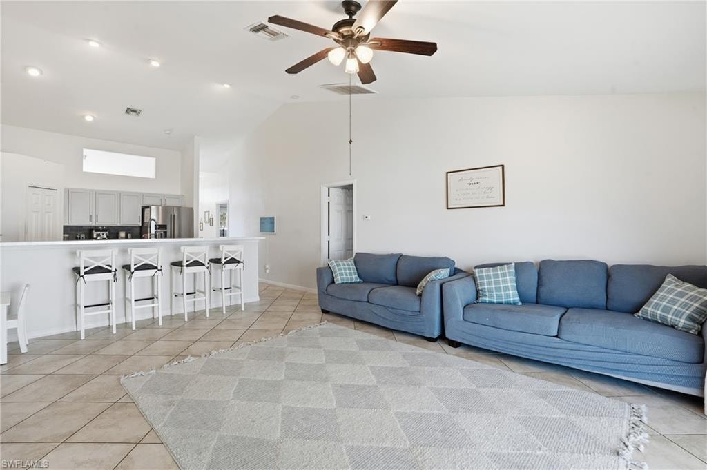 Living room with high vaulted ceiling, light tile patterned floors, and ceiling fan