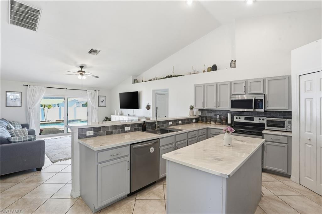 Kitchen with gray cabinets, open floor plan, a center island, appliances with stainless steel finishes, and high vaulted ceiling