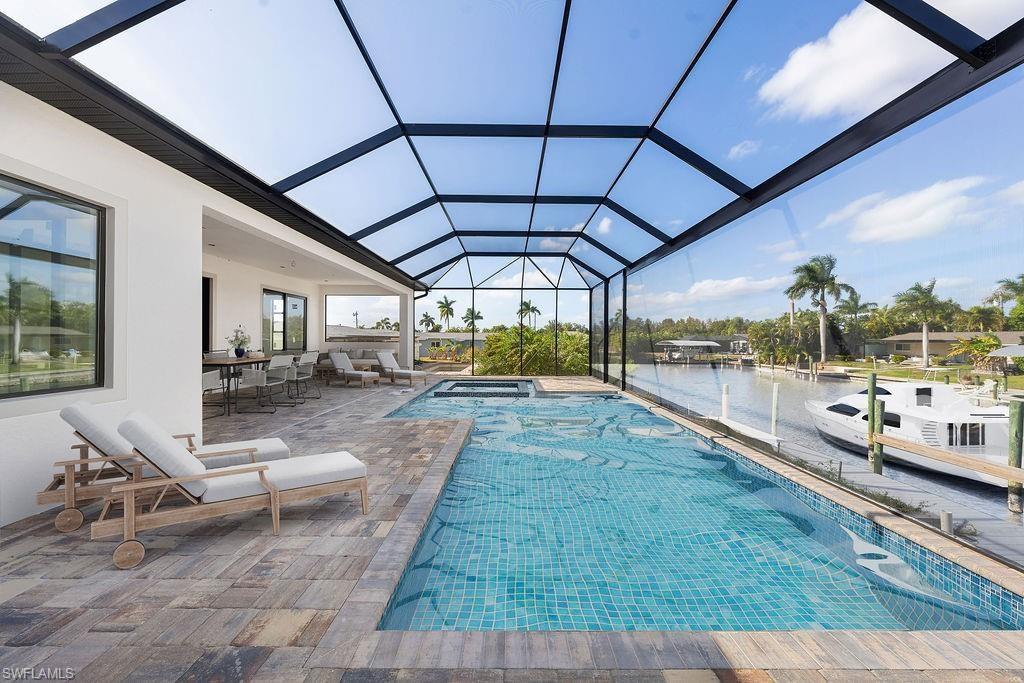 View of pool with a sunroom, glass enclosure, a patio, a water view, and a pool with connected hot tub