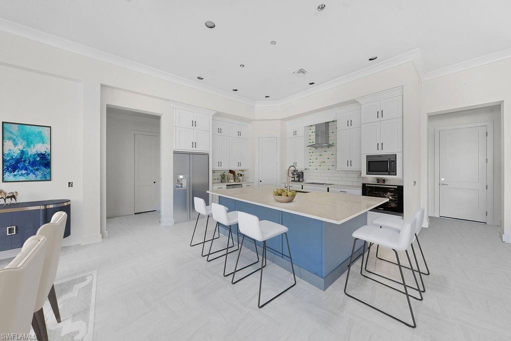 Kitchen featuring white cabinets, a kitchen breakfast bar, appliances with stainless steel finishes, a spacious island, and crown molding