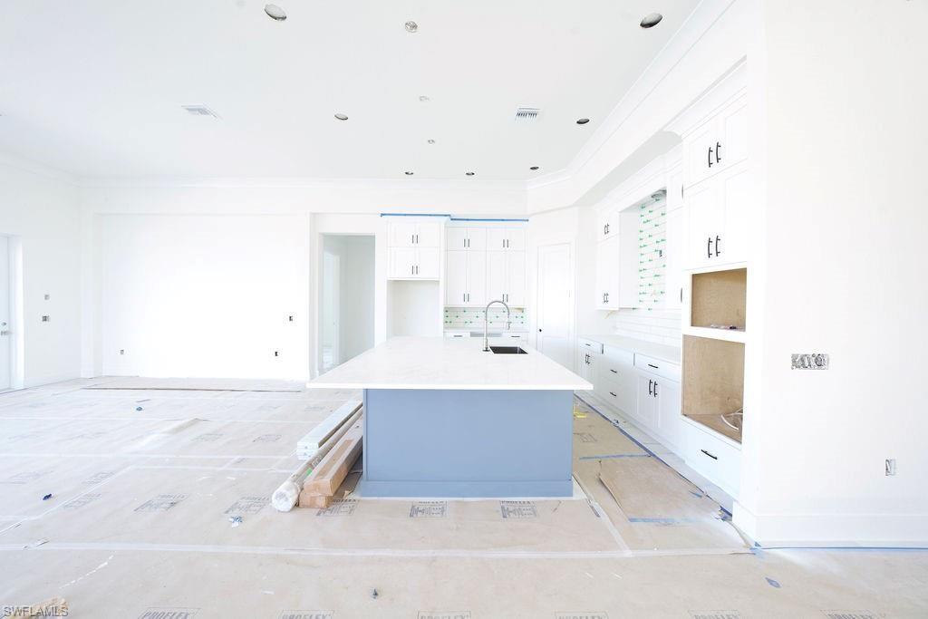 Kitchen with white cabinets, an island with sink, a breakfast bar area, crown molding, and light stone counters