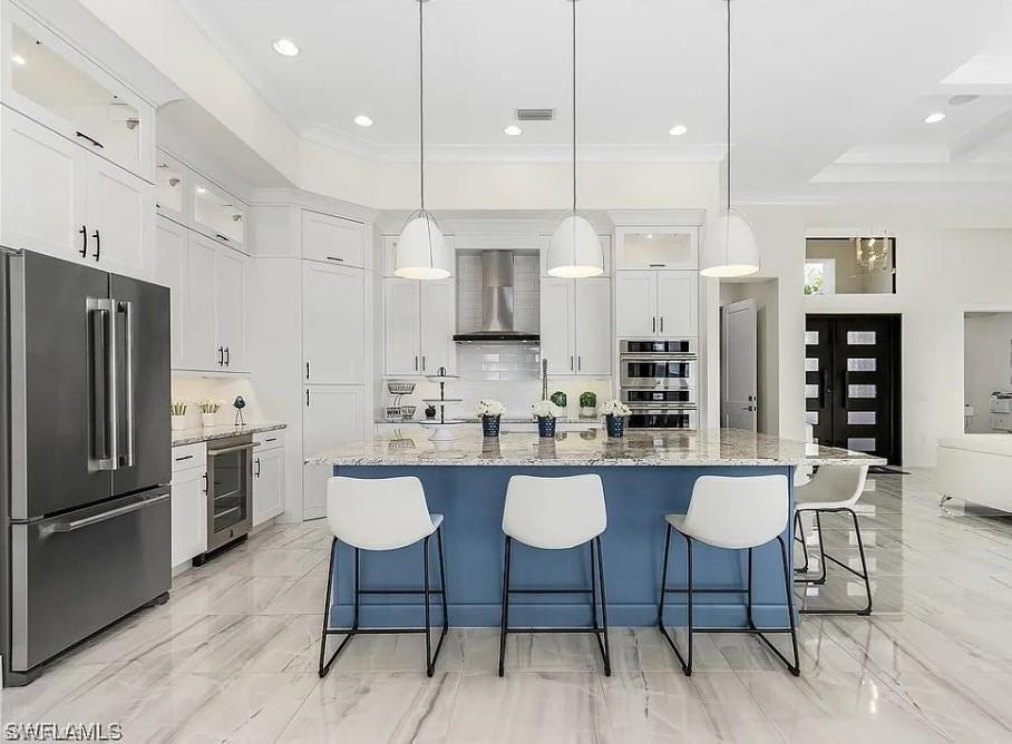 Kitchen featuring stainless steel appliances, a spacious island, white cabinetry, light stone countertops, and glass insert cabinets