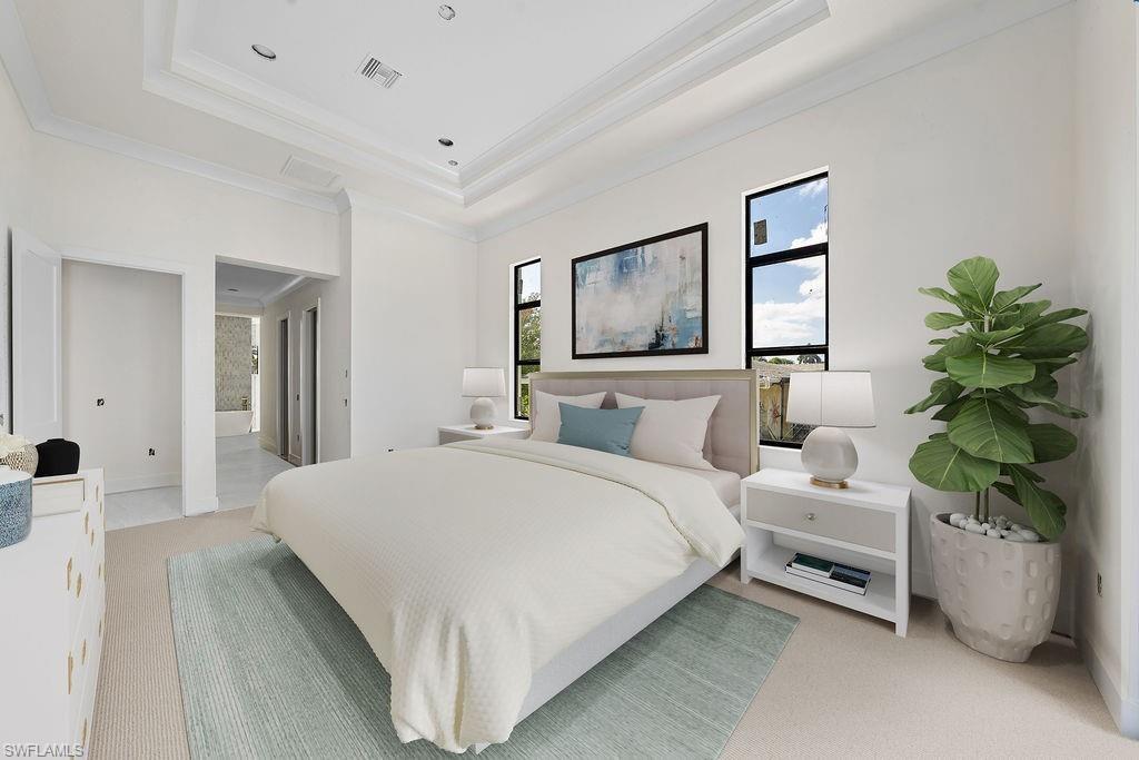 Bedroom with crown molding, light colored carpet, a tray ceiling, and ensuite bath