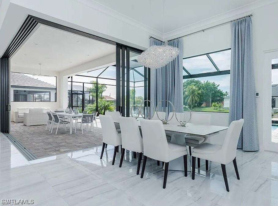 Dining space featuring ornamental molding, a chandelier, plenty of natural light, and light marble finish flooring