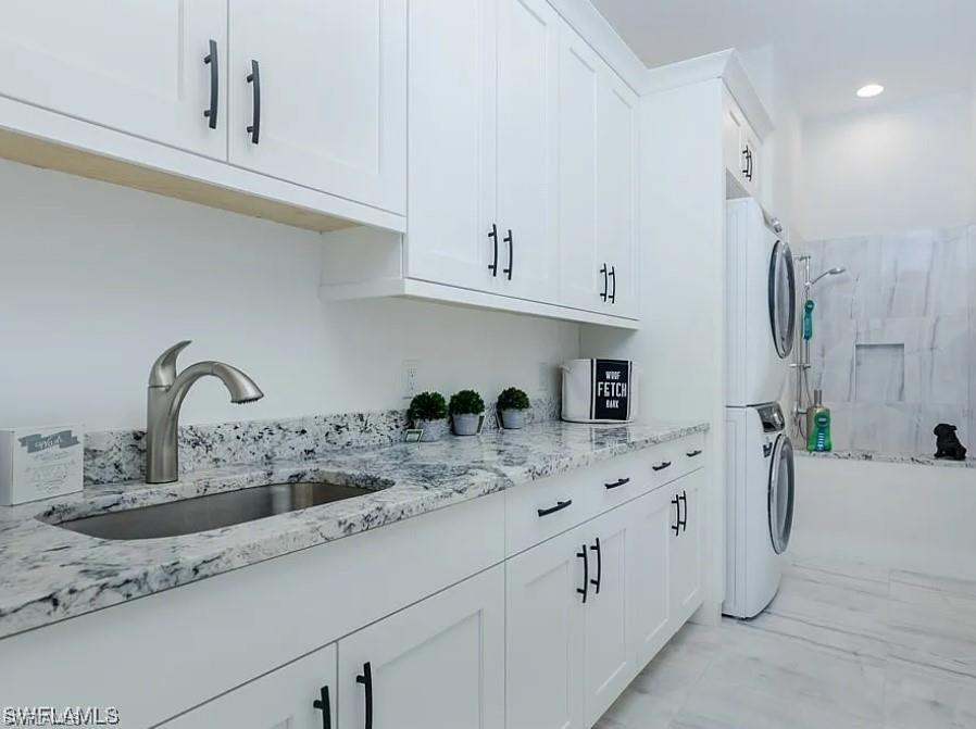 Washroom with estacked washer and dryer, light marble finish floors, and recessed lighting