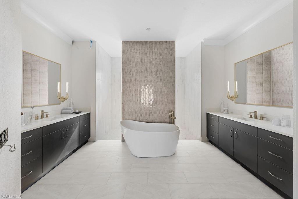 Full bathroom featuring a freestanding tub, two vanities, and light tile patterned flooring