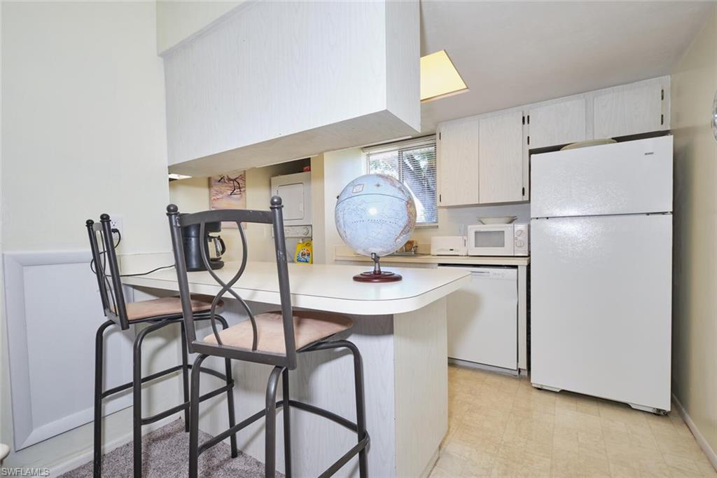 Kitchen featuring white appliances, light countertops, a kitchen bar, a peninsula, and light flooring
