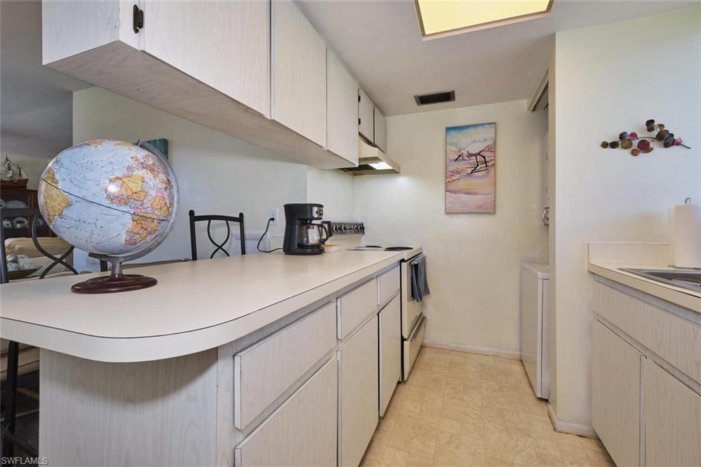 Kitchen with electric stove, light countertops, a breakfast bar, under cabinet range hood, and a sink