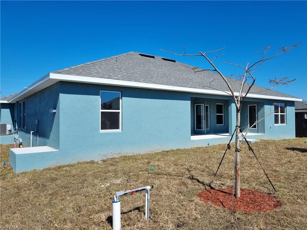 Rear view of house featuring stucco siding, a lawn, a patio area, and roof with shingles