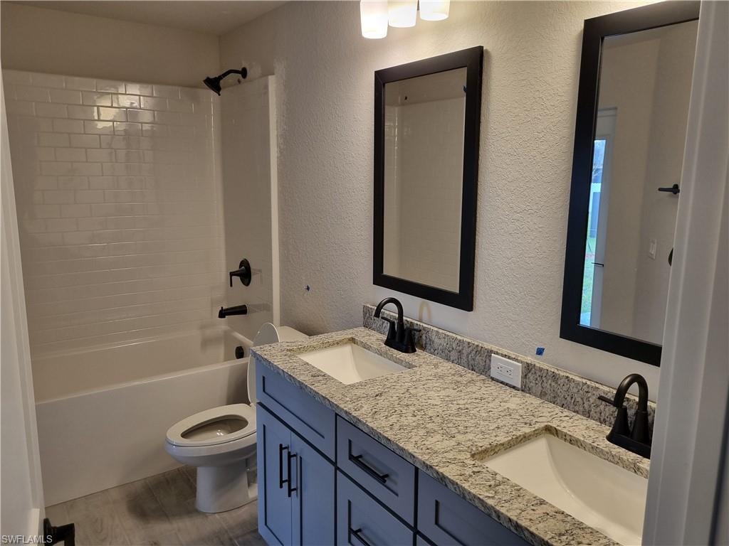 Bathroom featuring a textured wall, double vanity, bathing tub / shower combination, and light wood finished floors