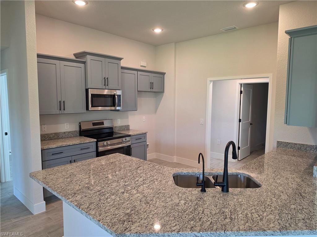 Kitchen featuring a stone-finish countertop island with a built-in sink, a black gooseneck faucet, and a separate water dispenser