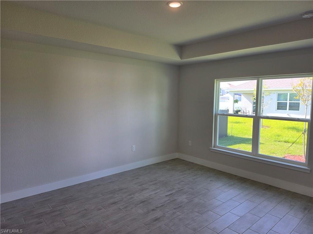 Spacious room featuring a tray ceiling with recessed lighting, wood-finish tile flooring, and a large window