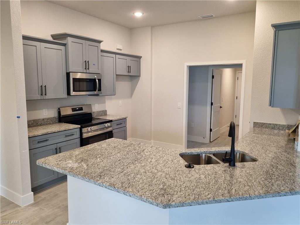 Kitchen featuring gray cabinets, stainless steel appliances, a peninsula, light stone countertops, and light wood finished floors