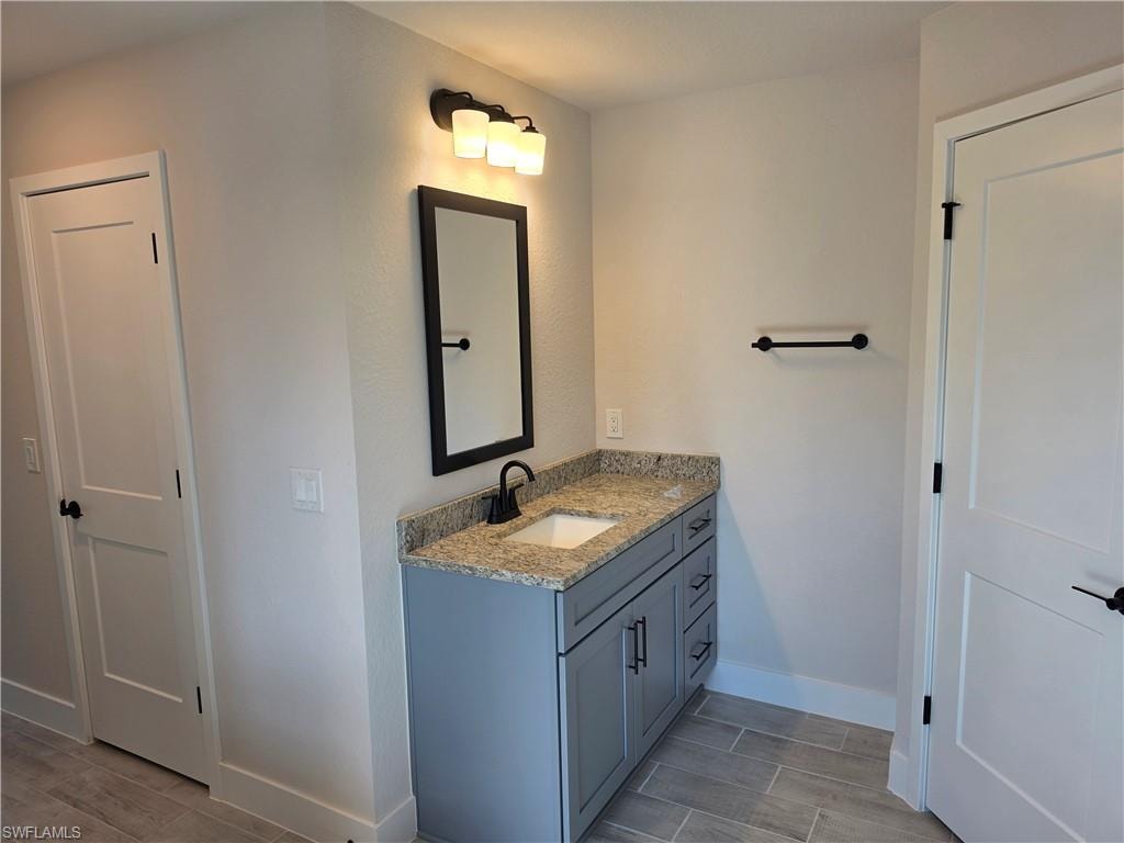 Bathroom vanity featuring a light gray cabinet, granite countertop, undermount sink, and matte black faucet