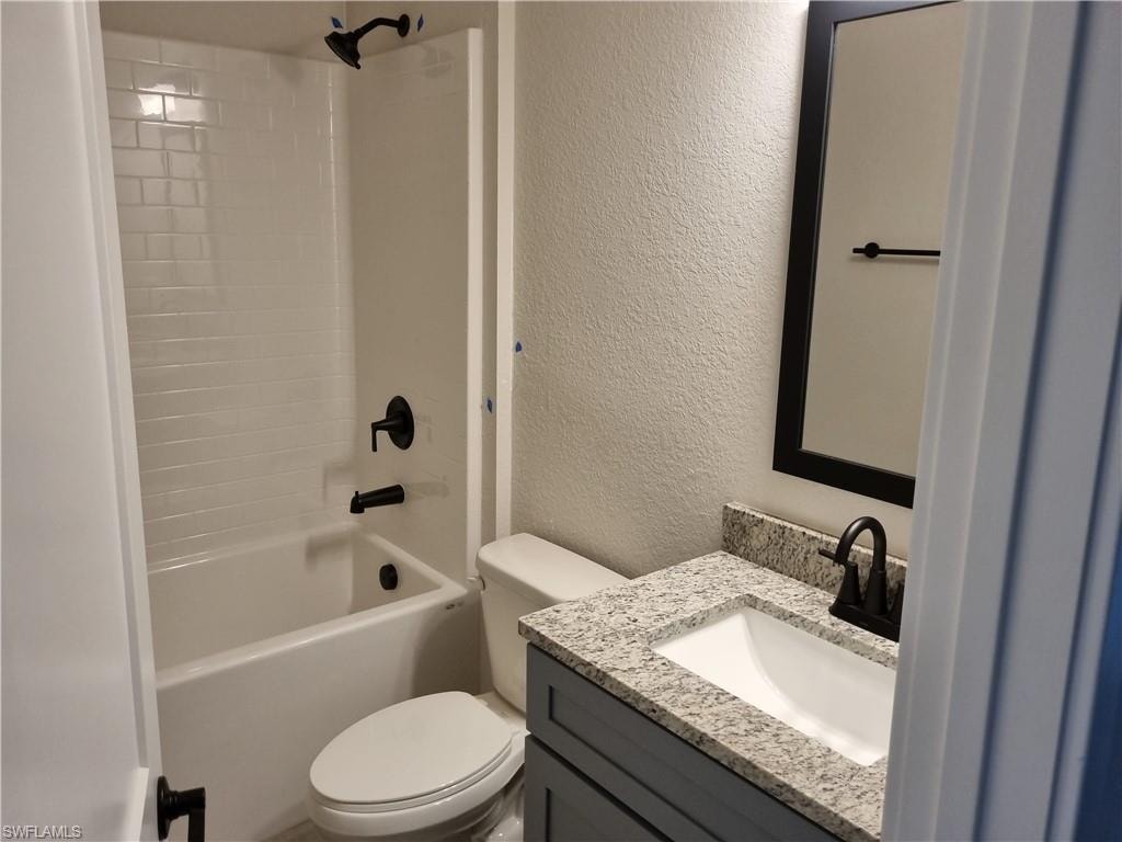 Full bathroom featuring a textured wall, vanity, and bathtub / shower combination