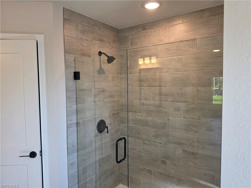 Glass-enclosed shower featuring large format wood-look tile, matte black fixtures, recessed lighting, and a linear vanity light fixture