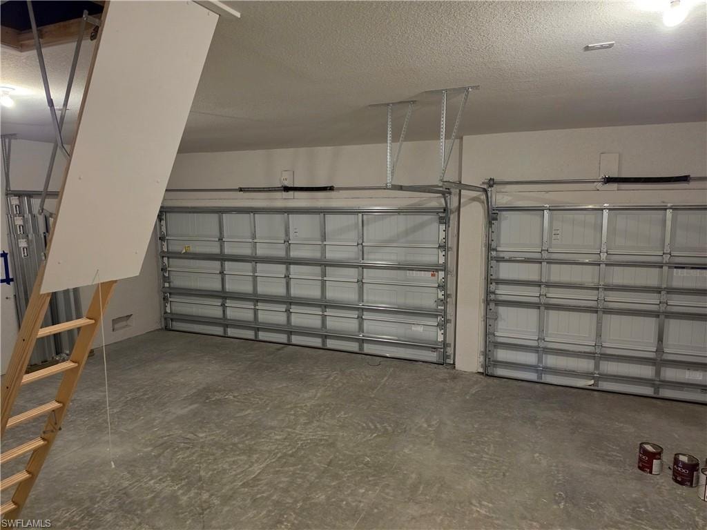 Two-car garage featuring segmented metal doors, concrete flooring, and an attic access ladder
