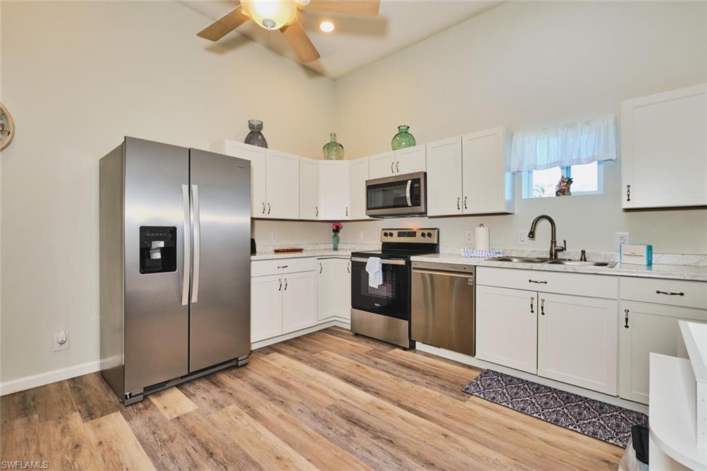 Kitchen of apartment on first level with appliances with stainless steel finishes, white cabinets, light wood-style floors, ceiling fan, and a high ceiling