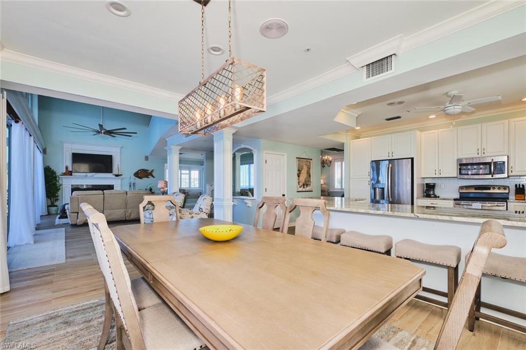Main Dining space featuring a ceiling fan, decorative columns, light wood-type flooring, a fireplace, and crown molding