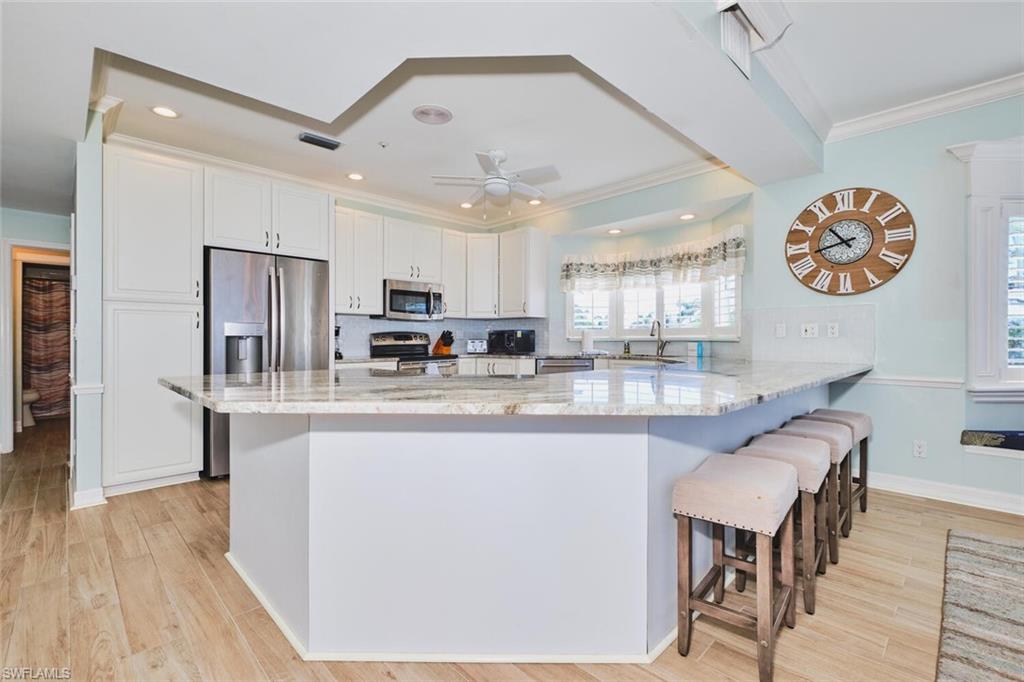 Main Kitchen with light stone counters, white cabinets, tasteful backsplash, a breakfast bar area, and a peninsula