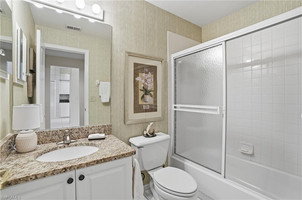 Full bath with wallpapered walls, vanity, and enclosed tub / shower combo