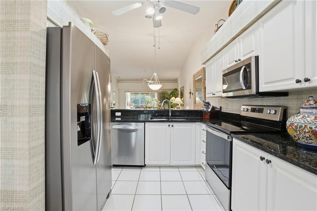 Kitchen featuring stainless steel appliances, dark stone counters, white cabinets, light tile patterned flooring, and lofted ceiling