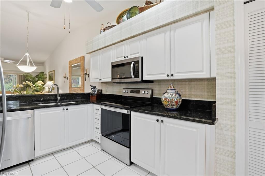 Kitchen featuring stainless steel appliances, vaulted ceiling, white cabinetry, hanging light fixtures, and decorative backsplash