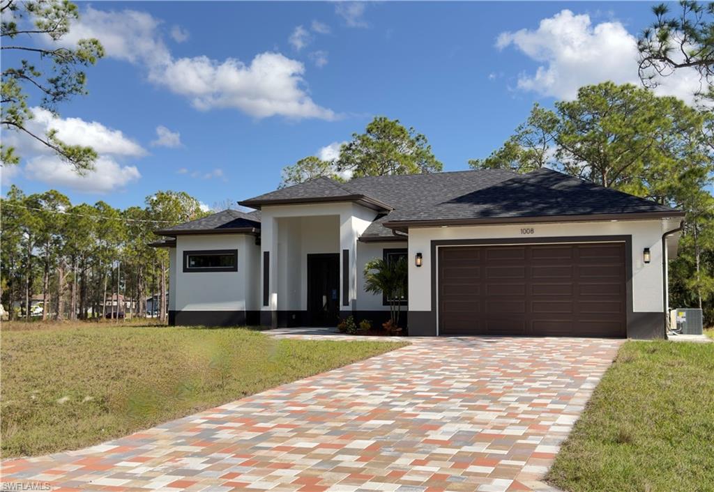 Prairie-style house featuring stucco siding, decorative driveway, a front lawn, a garage, and roof with shingles