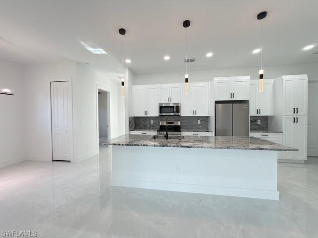 Kitchen featuring white cabinetry, dark stone counters, hanging light fixtures, stainless steel appliances, and decorative backsplash