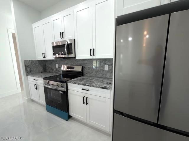 Kitchen with stainless steel appliances, dark stone countertops, white cabinets, and tasteful backsplash