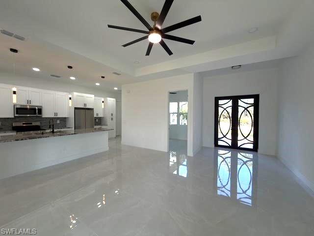 Unfurnished living room with a raised ceiling, recessed lighting, french doors, and ceiling fan