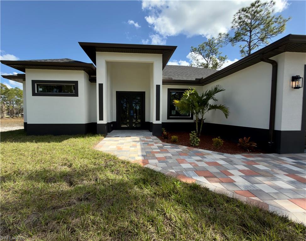 Entrance to property with a yard, a shingled roof, stucco siding, and french doors