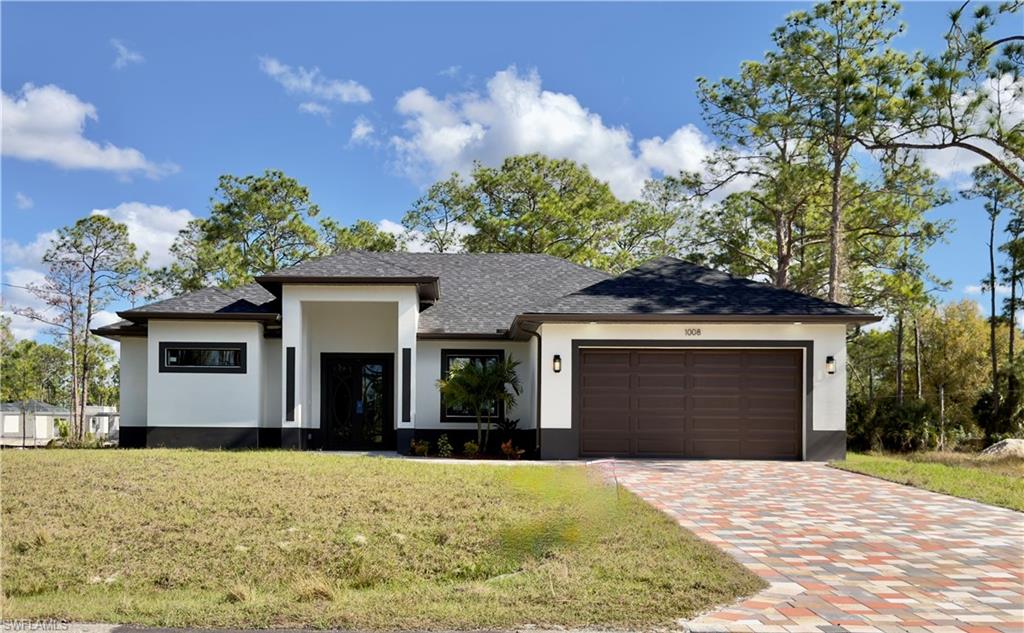 Prairie-style home featuring stucco siding, roof with shingles, decorative driveway, a front yard, and an attached garage