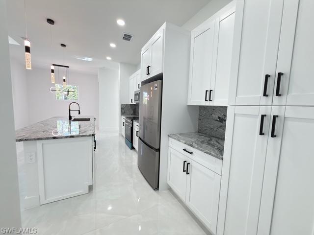 Kitchen with hanging light fixtures, light stone countertops, decorative backsplash, white cabinetry, and recessed lighting