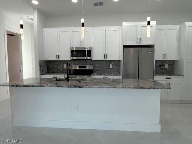 Kitchen with appliances with stainless steel finishes, hanging light fixtures, backsplash, dark stone countertops, and recessed lighting