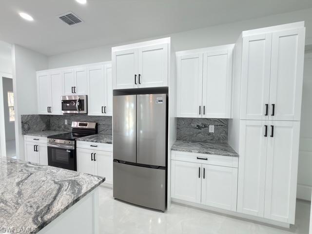 Kitchen featuring light stone countertops, appliances with stainless steel finishes, white cabinetry, and recessed lighting