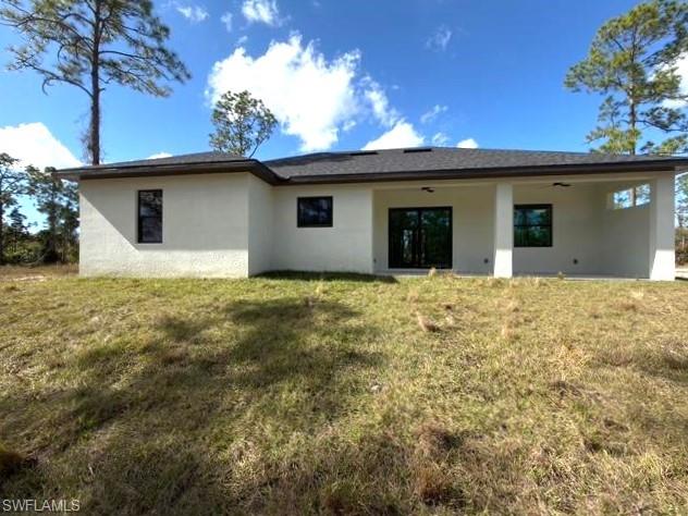 Rear view of house with stucco siding, a yard, and a patio