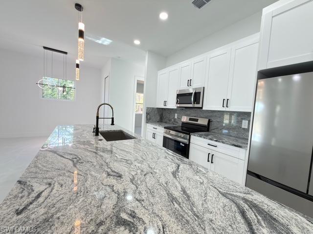 Kitchen featuring light stone counters, appliances with stainless steel finishes, white cabinets, decorative backsplash, and recessed lighting