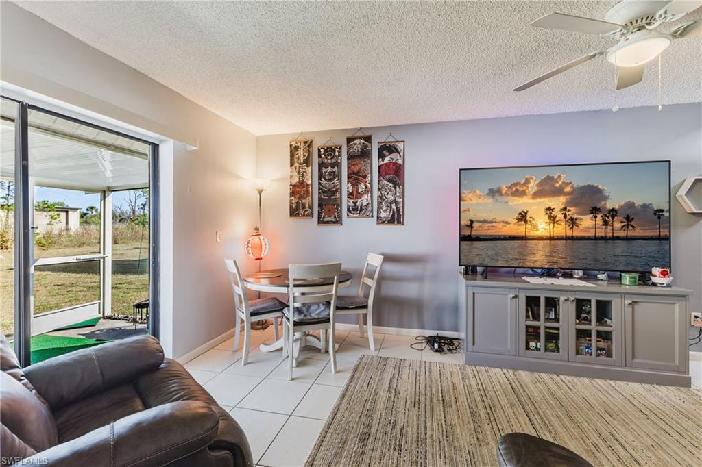 Living room featuring a ceiling fan, light tile patterned flooring, and a textured ceiling