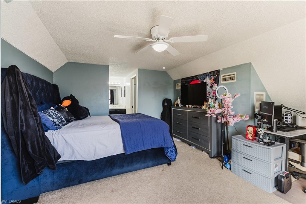Carpeted bedroom with vaulted ceiling, a textured ceiling, ceiling fan, and ensuite bath