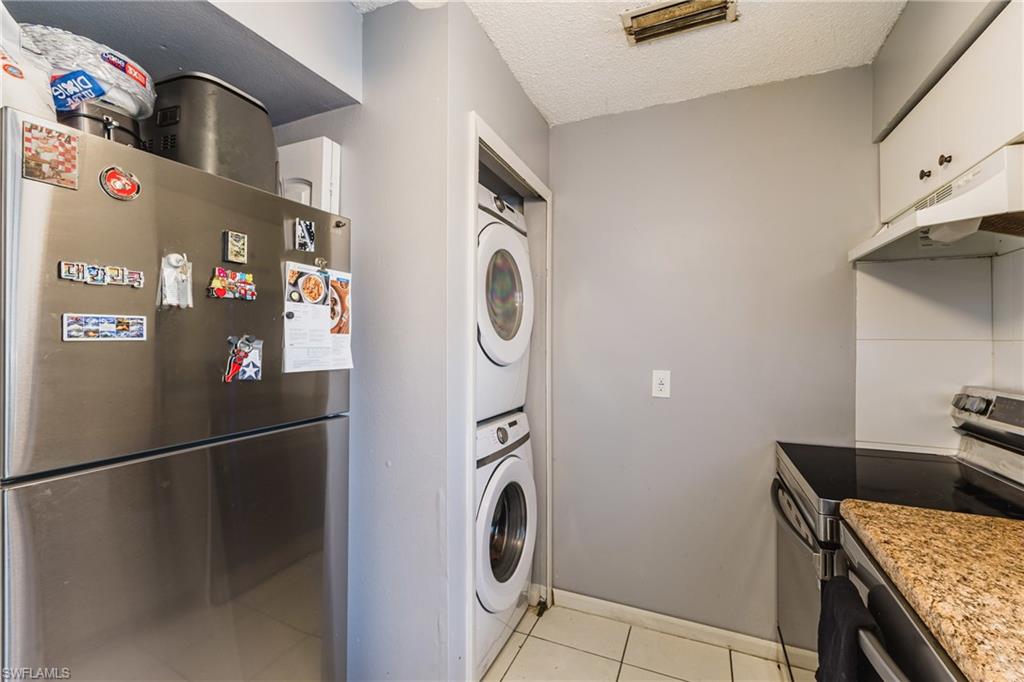 Kitchen featuring appliances with stainless steel finishes, under cabinet range hood, estacked washer and dryer, a textured ceiling, and light tile patterned floors