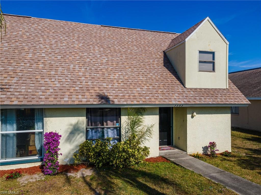View of front of home featuring roof with shingles, stucco siding, and a front yard