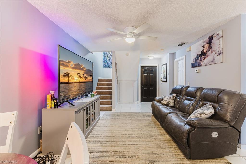 Living room with stairway, light tile patterned floors, ceiling fan, and a textured ceiling