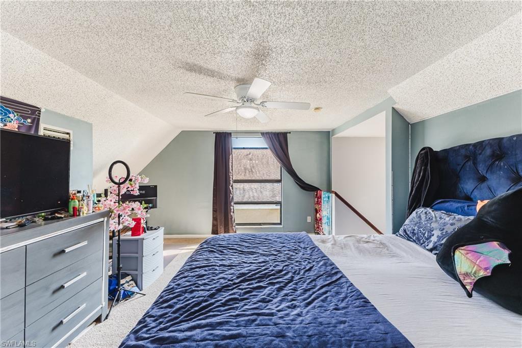 Carpeted bedroom with vaulted ceiling, ceiling fan, and a textured ceiling